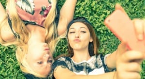 Two pretty girls taking a self portrait - Young women with a sportive casual outfit lying on meadow and having fun while taking a selfie