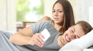 Jealous woman spying her husband mobile phone while he is reading a message